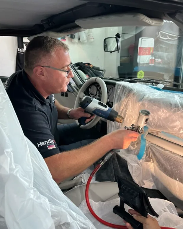 Fachmann von Alex Autopflege trägt mit der Spritzpistole neue Lederfarbe auf — professionelle Neufärbung im Studio