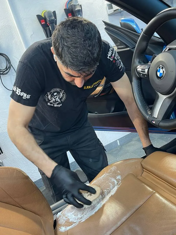 Gründliche Tiefenreinigung der Ledersitzfläche eines BMW mit Bürste und Reinigungsschaum