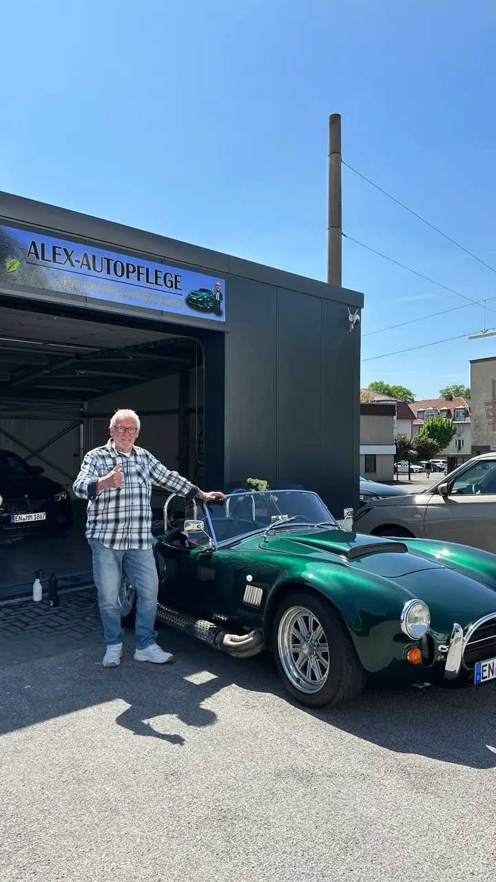 Zufriedener Kunde mit grünem Oldtimer-Roadster vor dem Studio von Alex-Autopflege in Schwelm